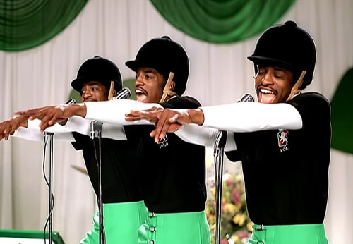 From the "Hey Ya" music video. Andre 3000 is dressed as his own backup singers in an equestrian outfit,  wearing green pants, black shirt and black helmet.